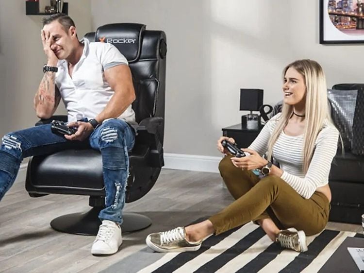 X Rocker -tuolissa istuva mies ja lattialla istuva nainen pelaavat yhdessä konsolipeliä