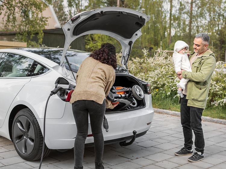 Nainen, lapsi ja mies seisovat latauksessa olevan sähköauton luona