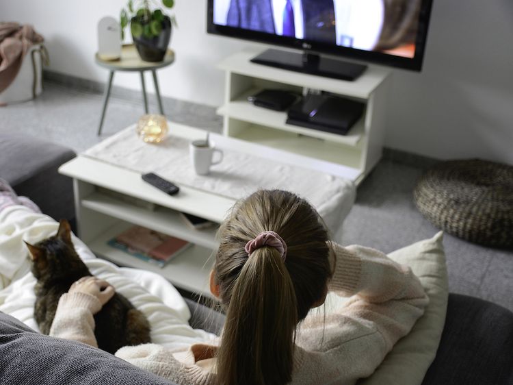 Nainen istuu sohvalla ja katsoo TV:tä kissa vierellään