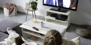 Nainen istuu sohvalla ja katsoo TV:tä kissa vierellään
