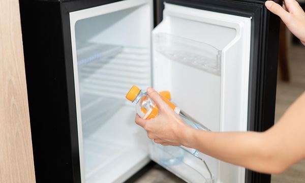 Naisen käsi pitelee pienestä mustasta jääkaapista otettua vesipulloa