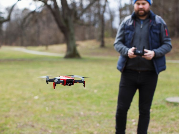 Mies seisoo puistossa ja lennättää dronea.
