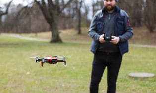 Mies seisoo puistossa ja lennättää dronea.