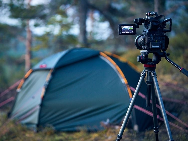 Camera on tripods standing in a forest pointing towards a tent