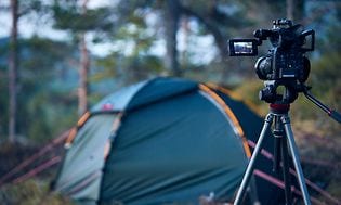 Camera on tripods standing in a forest pointing towards a tent