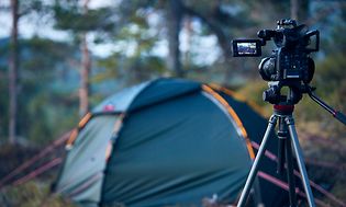 Camera on tripods standing in a forest pointing towards a tent