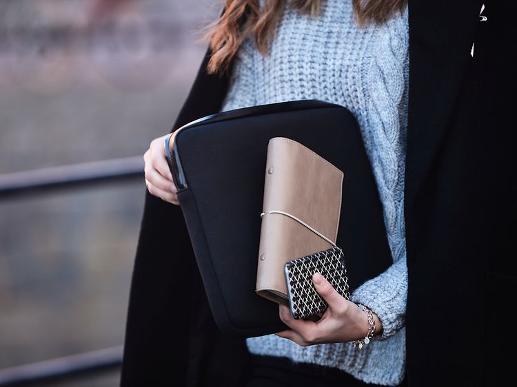 Nainen kantaa kannettavaa suojakuoressa ja pitelee käsilaukkua ja puhelinta