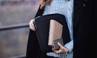Nainen kantaa kannettavaa suojakuoressa ja pitelee käsilaukkua ja puhelinta