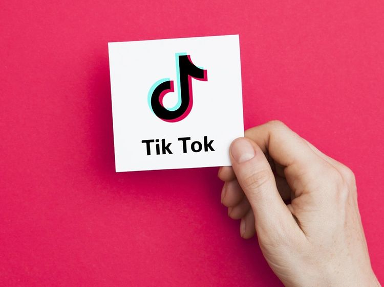 Käsi pitelee valkoista korttia, jossa on TikTok-logo ja takana vaaleanpunainen tausta