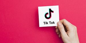 Käsi pitelee valkoista korttia, jossa on TikTok-logo ja takana vaaleanpunainen tausta