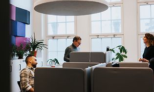 Kaksi miestä ja nainen työskentelevät avoimessa toimistoympäristössä