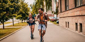 Mies ja nainen ajavat sähköpotkulaudoilla kaupungilla