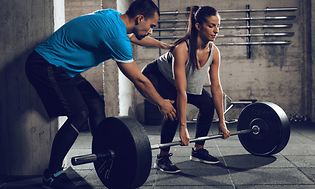 Nainen nostaa painoja personal trainerin avustuksella