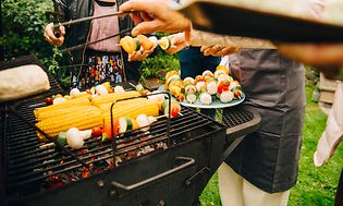 People standing around a charcoal grill grilling vegstables