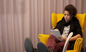 Nainen istuu keltaisessa tuolissa iPad kädessään