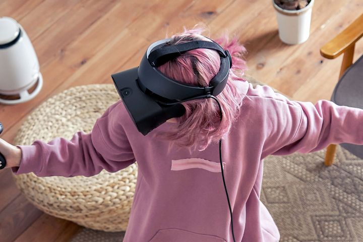 Nainen seisoo huoneen keskellä VR-lasit päässään ja pelaa VR-peliä