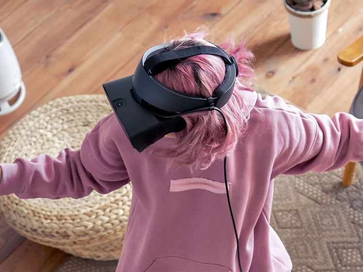 Nainen seisoo huoneen keskellä VR-lasit päässään ja pelaa VR-peliä