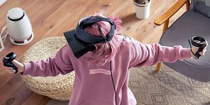 Nainen seisoo huoneen keskellä VR-lasit päässään ja pelaa VR-peliä