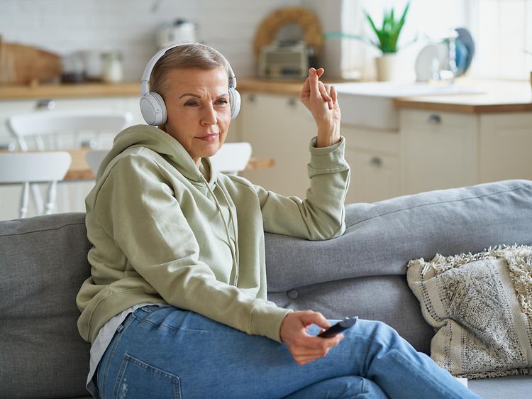 Nainen istuu sohvalla langattomat kuulokkeet päässä.