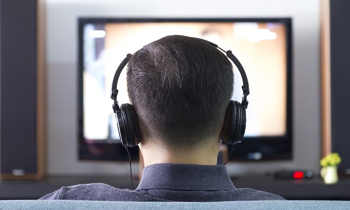 Mies katsoo televisiota kuulokkeet päässä.
