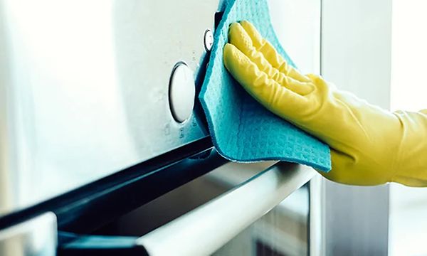 Suojahanskaan pukeutunut käsi pyyhkii uunin etupaneelia