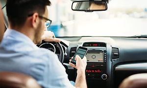 Autossa oleva mies katsoo älypuhelintaan