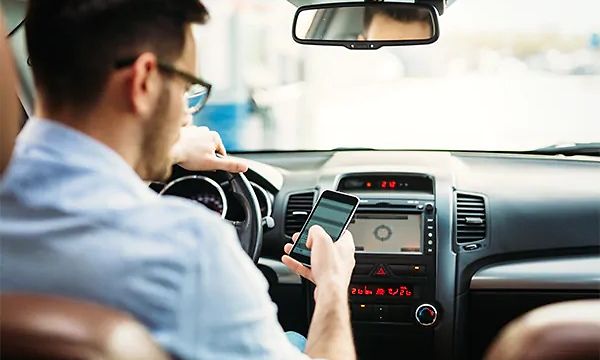 Autossa oleva mies katsoo älypuhelintaan