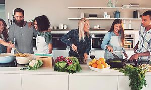Kuusi ihmistä kokkaa yhdessä suuressa keittiössä