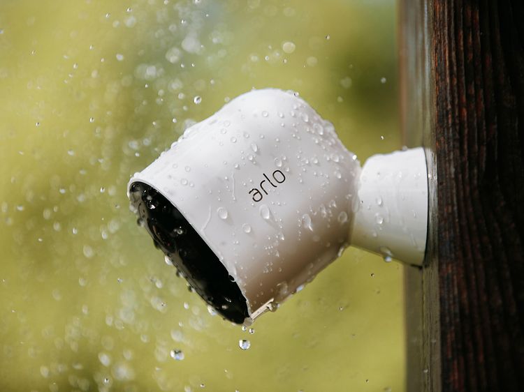 Valkoinen Arlo Pro 3 seinällä vesisateessa.