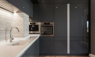 Harmaan ja valkoisen sävyinen minimalistisesti sisustettu keittiö integroiduilla kodinkoneilla