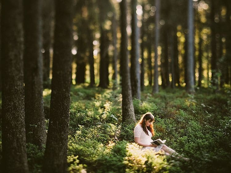 Valkoisiin vaatteisiin pukeutunut nainen lukee kirjaa metsässä