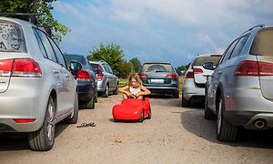 Tyttö punaisilla polkimilla varustetussa autossa tavallisten autojen välissä
