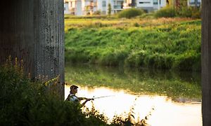 Mies kalastaa joessa betonisillan alla