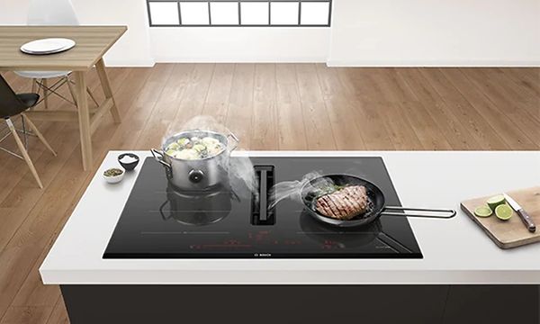 Bosch-keittotaso sisäänrakennetulla liesituulettimella, jonka vieressä valmistetaan ruokaa pihvistä ja vihanneksista