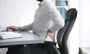 Toimistossa istuva mies pitelee särkevää selkäänsä