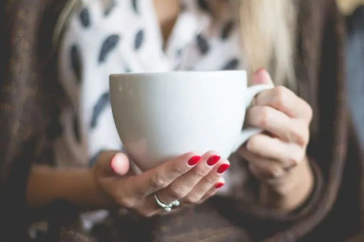 Lähikuva naisesta suuri kahvi kuppi kädessään 