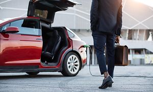 Salkkua kantava mies kävelee kohti latauksessa olevaa sähköautoa