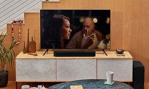 Sonos Beam 2 -soundbar ja TV-ruudulla nainen viinilasi kädessään