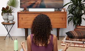 Sonos Beam (Gen 2) -soundbar ja television edessä joogaava nainen