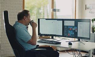 Mies istuu työskentelemässä tietokoneen ääressä ja juo kahvia kupista
