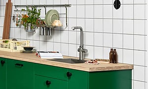 Epoq-keittiö, jossa vihreät kaapinovet ja puinen taso seikä säilytystilaa seinälle asennetussa telineessä