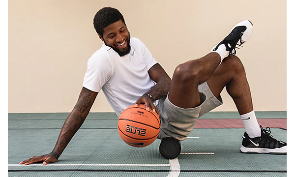 Urheilija Paul George istuu Theragun-laitteen päällä koripallo kädessään 