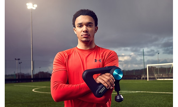 Trent Alexander Arnolds seisoo jalkapallokentällä Theragun-laite kädessään