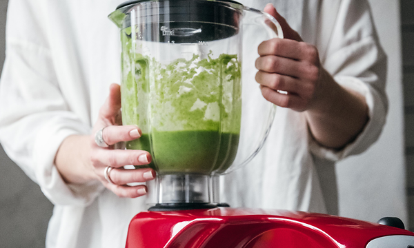 Henkilö tekee vihreää smoothieta punaisella tehosekoittimella