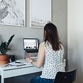 Nainen istuu työpöytänsä ääressä kotitoimistossa ja työskentelee kannettavan tietokoneen parissa