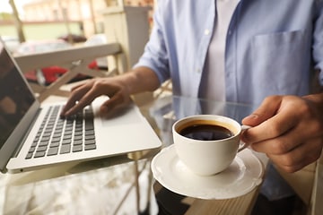 Tietokoneet - Korjaus - Henkilö juo kahvia kannettavan tietkoneen vieressä