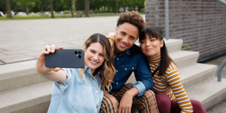 Fairphone 4 naisen kädessä joka ottaa ryhmäkuvan kahden muun kanssa