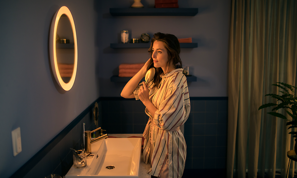 Nainen harjaa hiuksiaan Philips Hue Adore-peilin edessä.