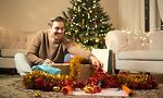 Mies istuu lattialla avaamassa joululahjoja