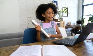 Kouluikäinen tyttö katsoo edessään olevaa kannettavaa tietokonetta oppikirja hänen edessään pöydällä